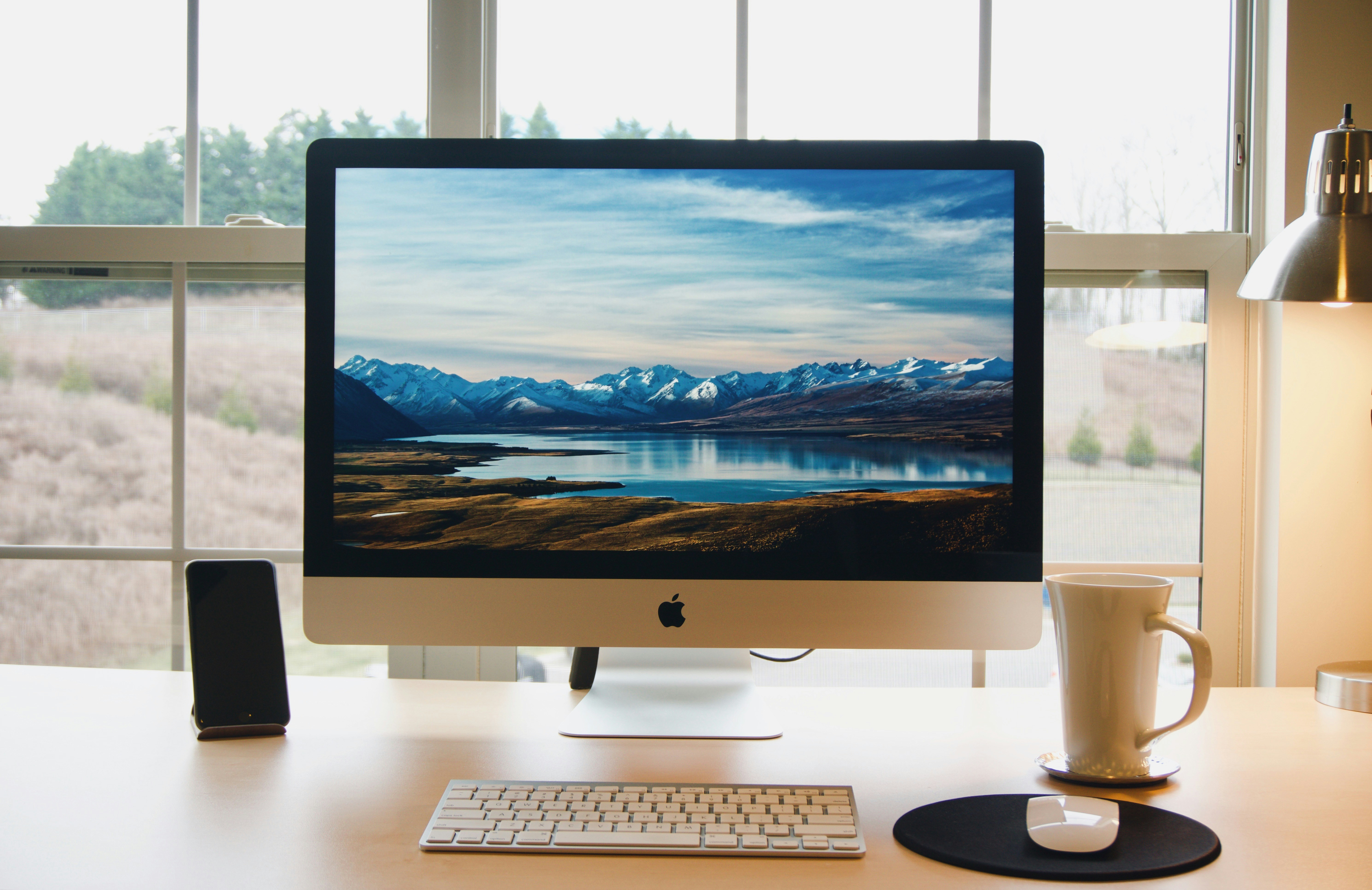 A computer sits on a desk along with a keyboard, a mouse, and a cup of coffee.